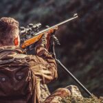 Poľovník pozoruje les cez moderný puškohľad počas rannej hliadky v prírode