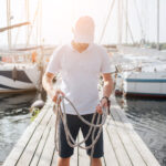 Námorník čistí plachtu a kontroluje laná na palube jachty počas údržby.