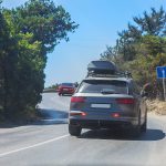 Auto so strešným boxom jazdí po horskej ceste počas letného dňa.