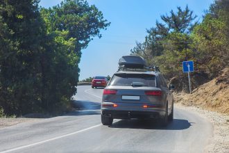 Auto so strešným boxom jazdí po horskej ceste počas letného dňa.